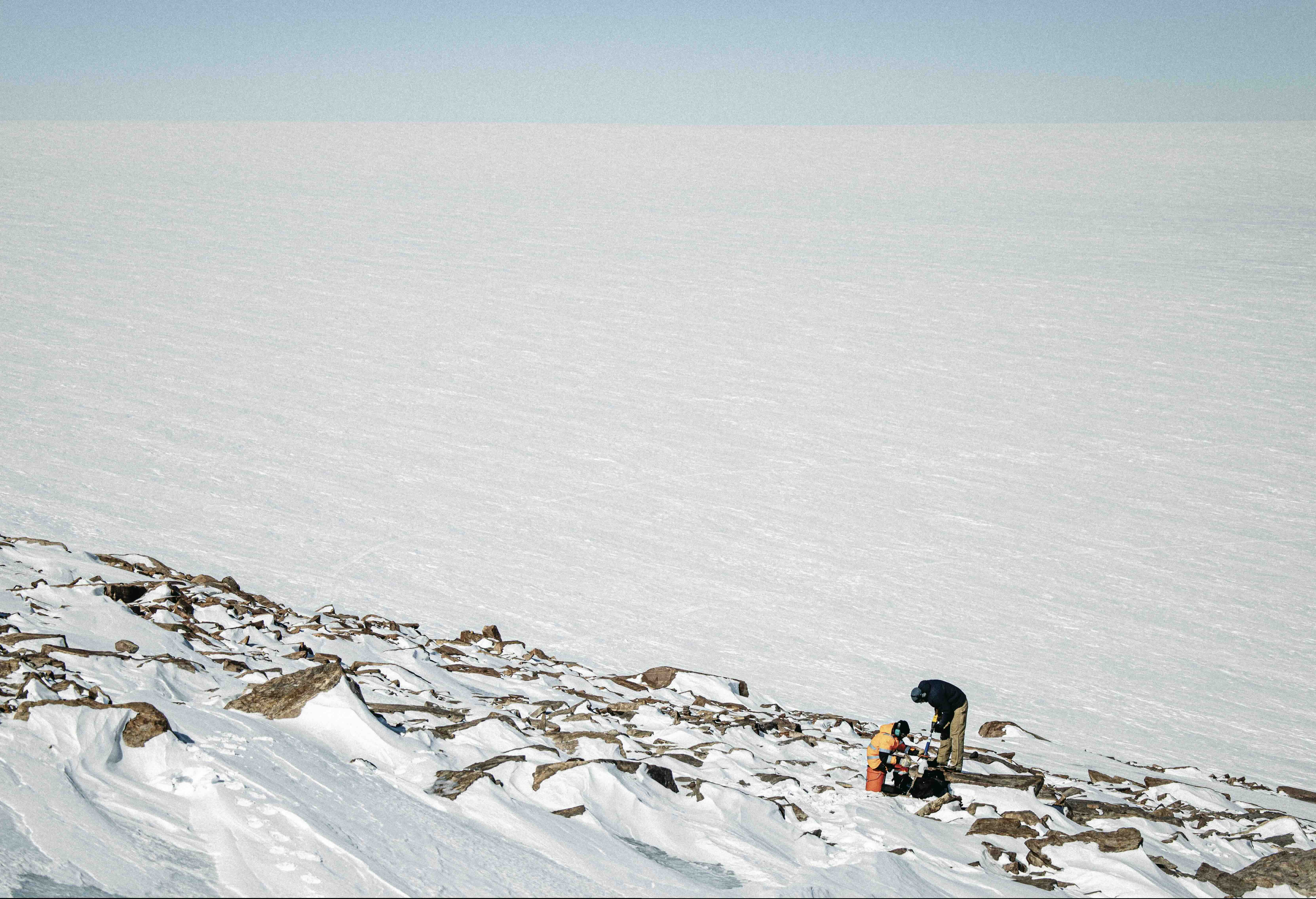 探索未知：2024年5月，探險隊成員沃爾科特─喬治和吉斯拉森用手持岩鑽，從格陵蘭冰蓋上一處冰原島峰的露頭中取出岩芯。他們取得的樣本可能有助解開一個關於地球氣候的大哉問：格陵蘭上一次綠意盎然是什麼時候？｜德爾維西奧（Jeffery Delviscio）